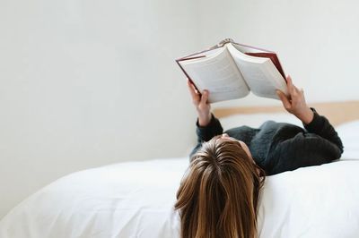 Woman reading book her bed.